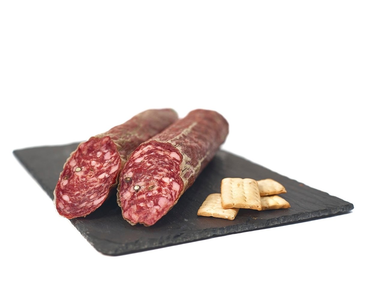 Dos salchichones curados cortados por la mitad sobre pizarra negra, con el corte a la vista y unas galletas saladas