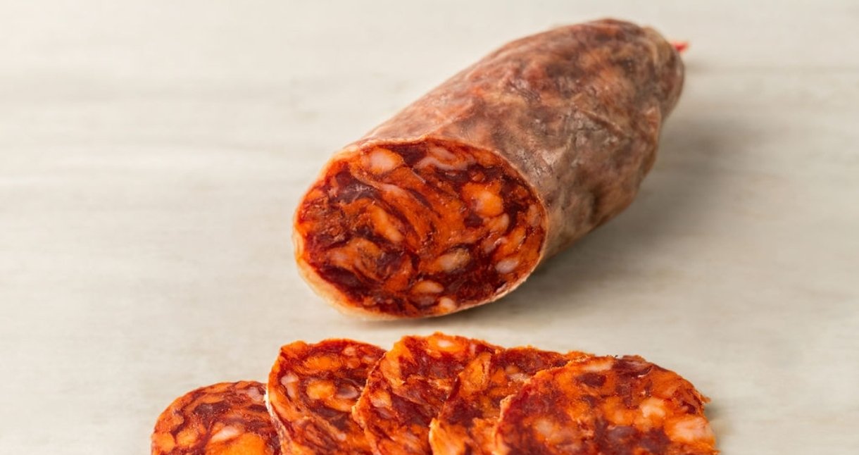 Chorizo curado cortado por la mitad y varias lonchas de chorizo sobre fondo claro
